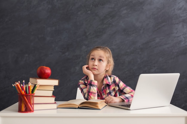 Bambina premurosa con il computer portatile. Bambino sveglio che fa i compiti sul computer. Moderno concetto di istruzione, comunicazione e tecnologia online, spazio di copia