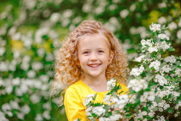 Bambina ridente sveglia divertente in primavera in un giardino fiorito