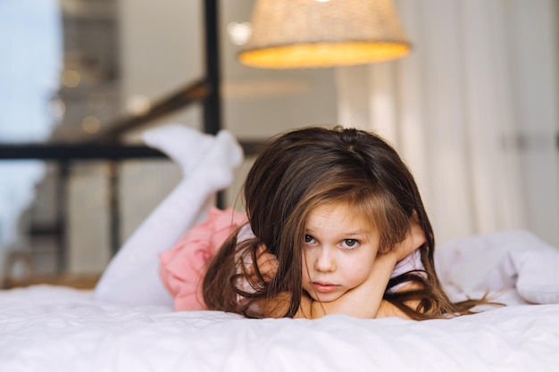 Bambina sdraiata nel letto guardando la telecamera