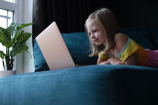 Bambina sdraiata sul divano e guardando lo schermo del laptop