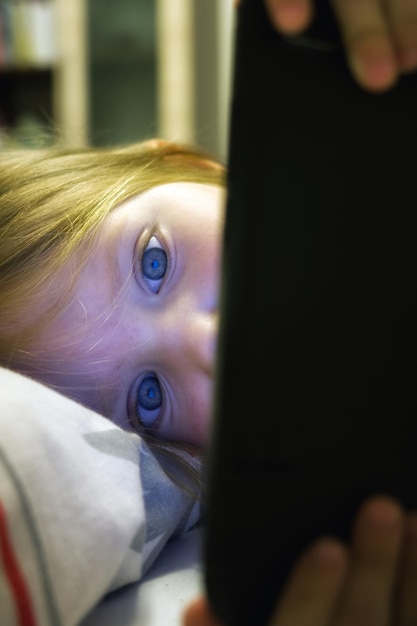 Bambina sdraiata sul letto con in mano uno smartphone e guardando sullo schermo