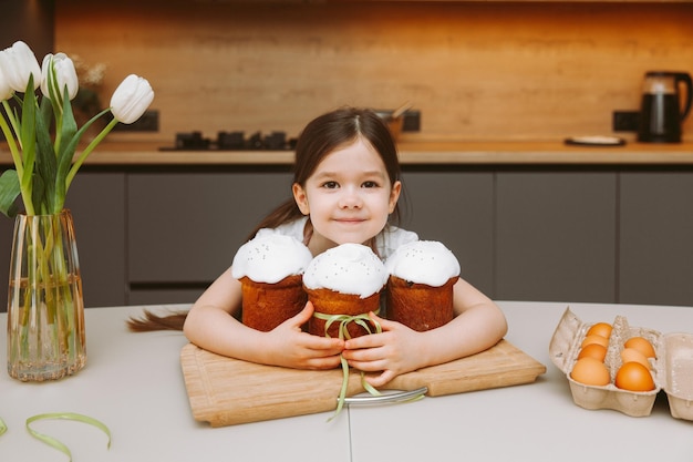Bambina seduta al tavolo con i biscotti di Pasqua Cristo è risorto Cottura fatta in casa per le vacanze cibo sano
