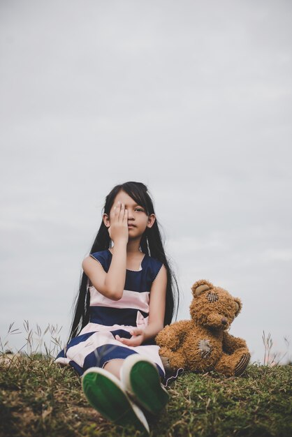 Bambina seduta con il suo orso sconvolto nei prati campo.