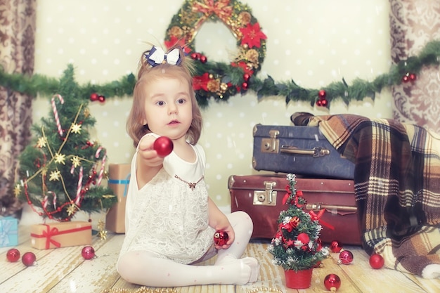 Bambina seduta davanti a un albero di Natale e gioca con i giocattoli