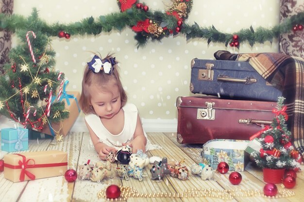 Bambina seduta davanti a un albero di Natale e gioca con i giocattoli