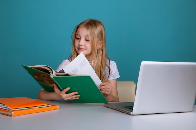 Bambina seduta in classe con il libro davanti al computer.