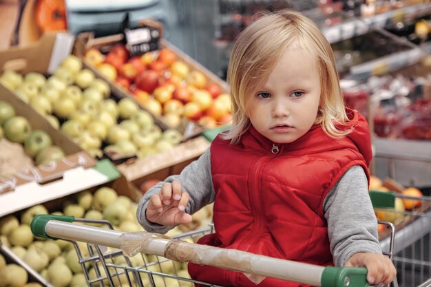 Bambina seduta nel carrello in negozio di frutta alimentare o supermercato