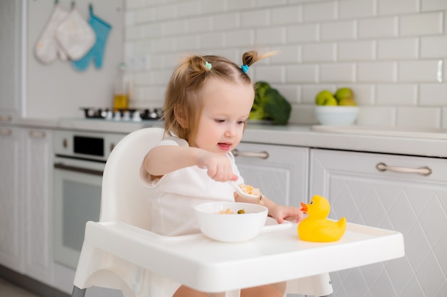 bambina seduta su un seggiolone a giocare con il porridge