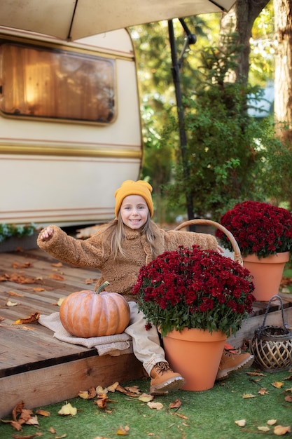 bambina seduta sul portico di casa con crisantemi in vaso e zucche.