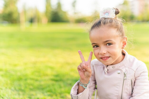 Bambina seduta sull'erba che mostra segno di pace o vittoria