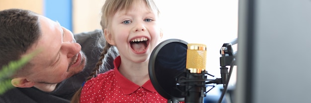 Bambina seduta sulle ginocchia di suo padre e cantando una canzone nella creatività dei bambini del microfono microphone