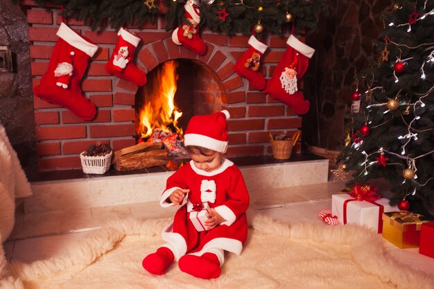 Bambina seduta vicino al camino e all'albero di Natale con scatole regalo