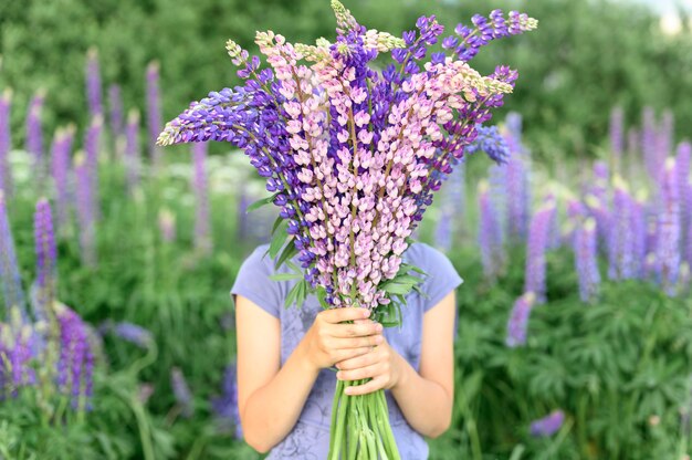 Bambina senza volto con bouquet di lupini fioriti