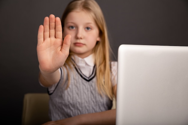 Bambina seria che mostra il segnale di stop isolato nella stanza buia.