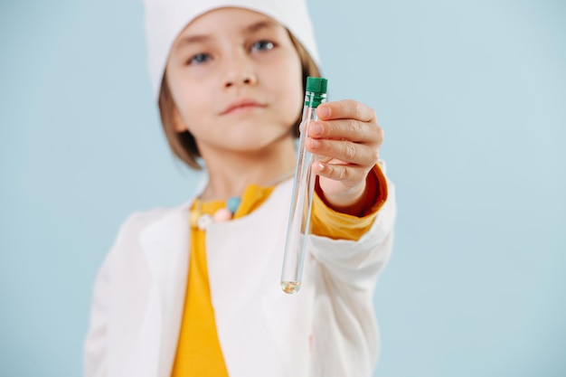 Bambina seria vestita con abiti bianchi e cappello con in mano una fiaschetta di vetro