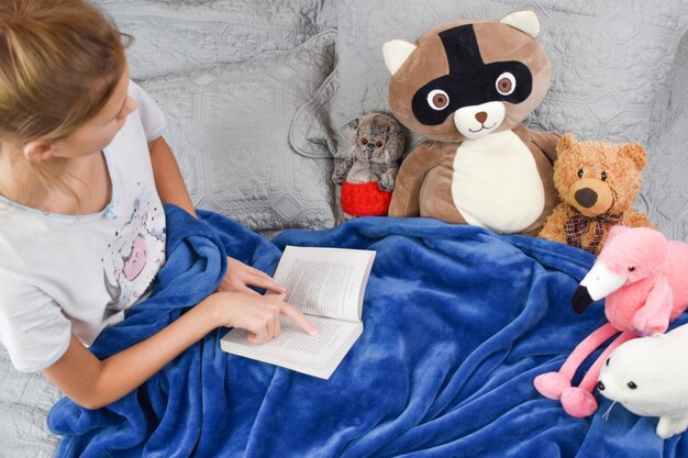 bambina si trova sul letto con un libro e giocattoli