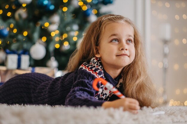 Bambina sognante che scrive una lettera a Babbo Natale, sdraiata sul flor in una stanza decorata, in attesa di regali e miracoli