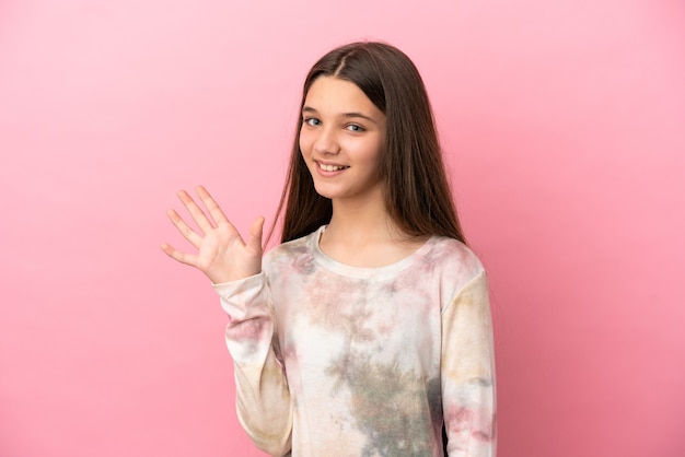 Bambina sopra fondo rosa isolato che saluta con la mano con l'espressione felice