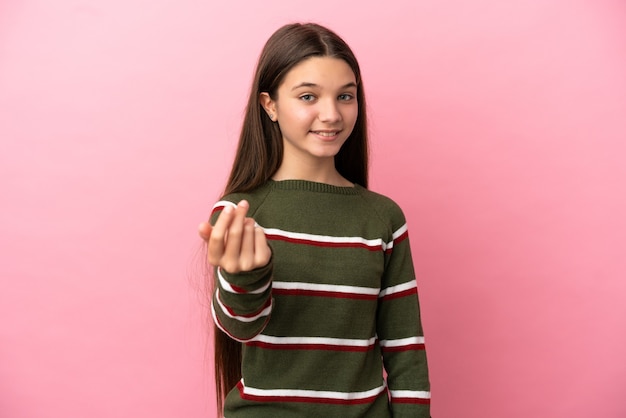 Bambina sopra il muro rosa isolato che invita a venire con la mano