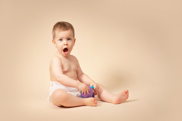 Bambina sorpresa che tiene pappe in una bottiglia con acqua nelle sue mani bambino sorridente in un bambino pannolino su uno sfondo solido monocromatico in studio mostra emozioni