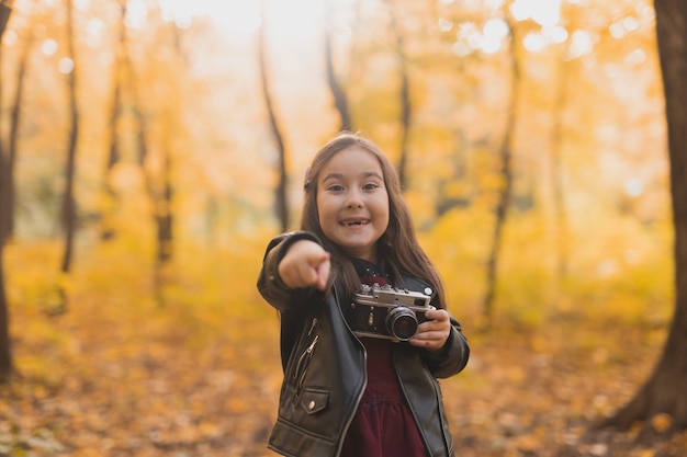 Bambina sorpresa che usa una macchina fotografica antiquata nella stagione autunnale del fotografo naturalista e