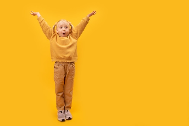 Bambina sorpresa in abiti gialli alzò le mani Ritratto a figura intera di sfondo giallo per bambini in età prescolare Spazio di copia