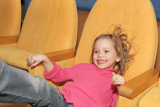 Bambina sorridente abbastanza felice sveglia che si siede nella sala del cinema