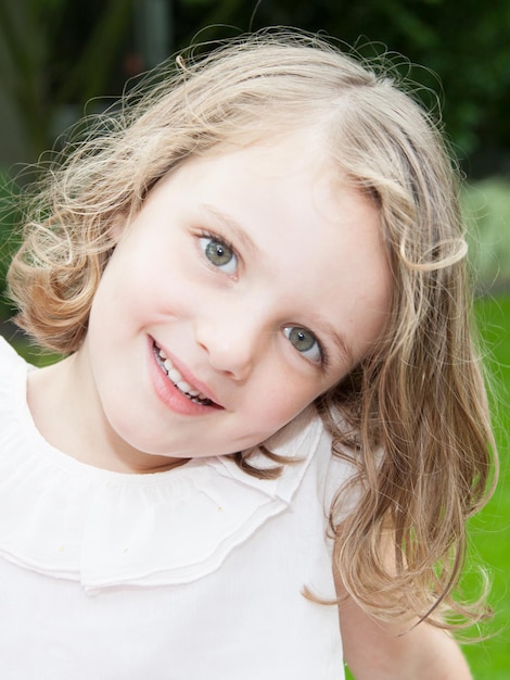 Bambina sorridente adorabile che si siede sull'erba nella giornata estiva all'aperto