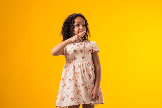 Bambina sorridente che indica un posto vuoto su uno sfondo giallo Concetto pubblicitario