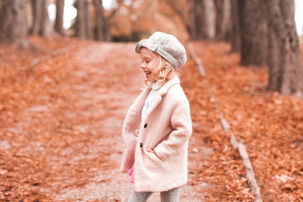 Bambina sorridente che indossa cappotto alla moda e berretto lavorato a maglia