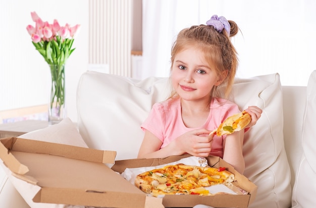 Bambina sorridente che mangia pizza, sul divano