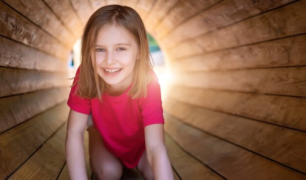 Bambina sorridente che si siede nel tubo di legno nel parco