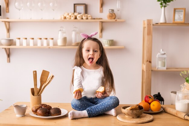 bambina sorridente che si siede sulla superficie di lavoro della cucina in attesa di colazione. Ragazza allegra e birichina in cucina.