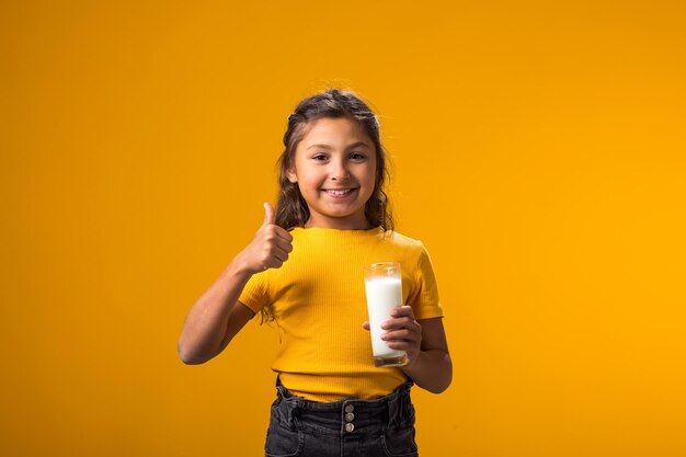 Bambina sorridente che tiene in mano un bicchiere di latte e mostra il pollice verso l'alto