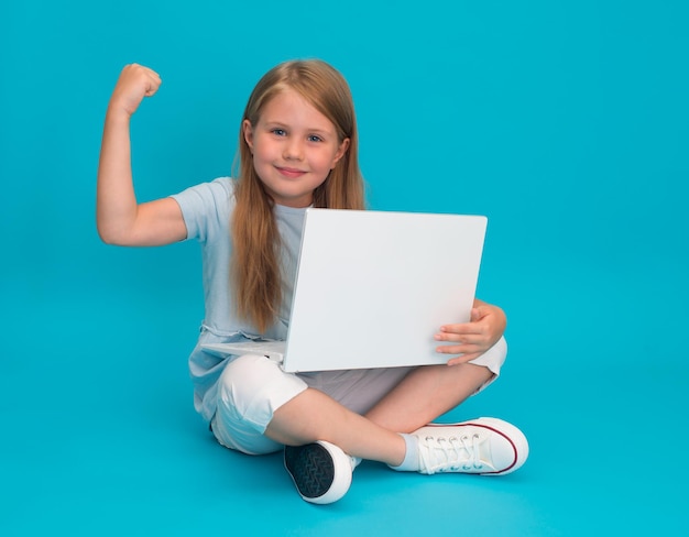 Bambina sorridente che usa il computer portatile e mostra il segno di forza che posso concetto