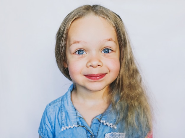 Bambina sorridente con gli occhi azzurri bella, su uno sfondo bianco