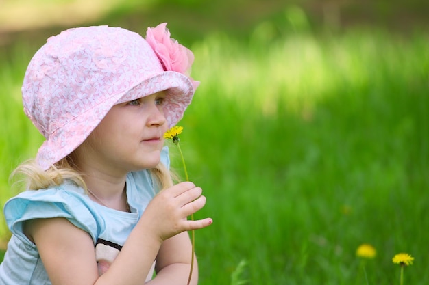 Bambina sorridente con il dente di leone su un'erba in un parco