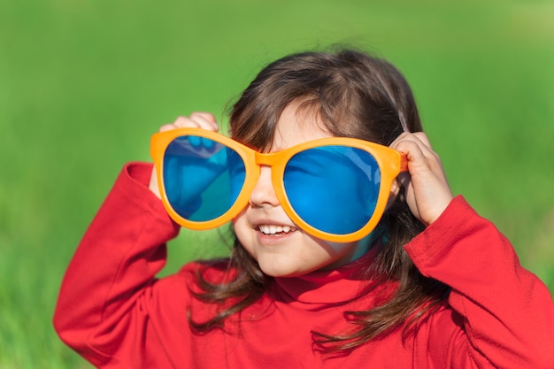 Bambina sorridente felice che indossa grandi occhiali da sole sul prato verde