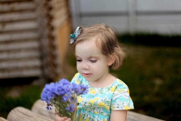 Bambina sorridente felice con i capelli rossi con il fiore al giorno d'estate all'aperto. Foto di alta qualità