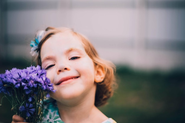 Bambina sorridente felice con i capelli rossi con il fiore al giorno d'estate all'aperto. Foto di alta qualità