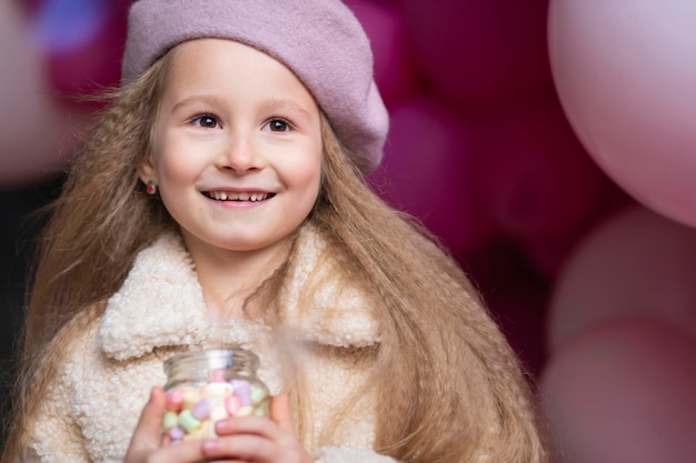 Bambina sorridente felice in berretto che gioca con i palloni rosa. bambino in vacanza. Festa di compleanno per bambini