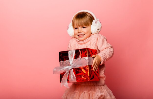 Bambina sorridente felice in cuffie invernali con una confezione regalo di Natale.