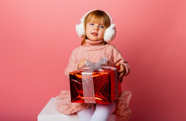 Bambina sorridente felice in cuffie invernali con una confezione regalo di Natale.