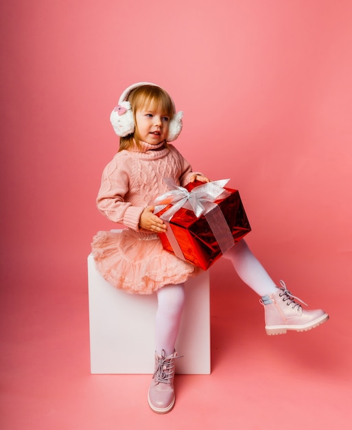 Bambina sorridente felice in cuffie invernali con una confezione regalo di Natale.