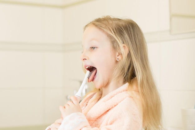 Bambina sorridente felice lavarsi i denti usando uno spazzolino elettrico ad ultrasuoni in bagno a casa orale ...