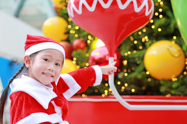Bambina sorridente in costume santa con sfondo di Natale. Buon Natale e felice