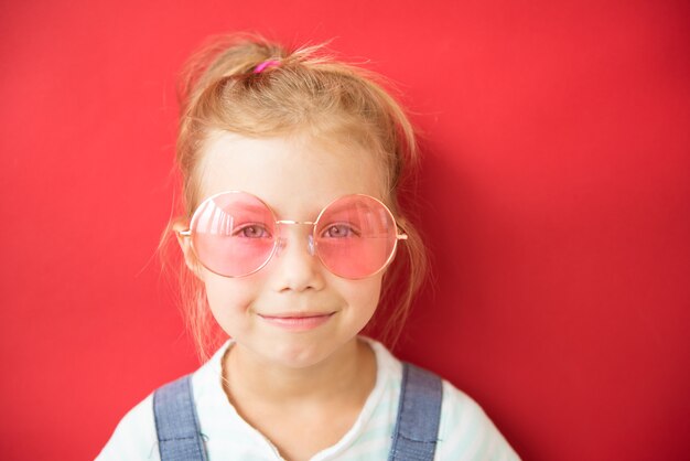 Bambina sorridente in grandi bicchieri rotondi rosa su sfondo rosso