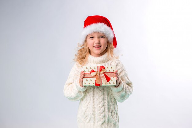 bambina sorridente in santa cappello tenendo confezione regalo su sfondo bianco