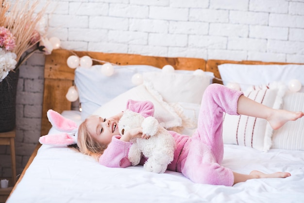 Bambina sorridente sdraiata a letto con l'orsacchiotto