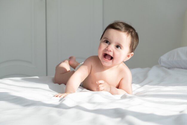 Bambina sorridente, sdraiato su un letto su lenzuola bianche in tuta bianca.